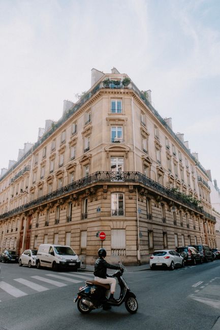 Classic corner building with a person on a scooter, surrounded by cars on an urban intersection.