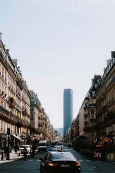 City street in Paris featuring Montparnasse Tower, bustling with cars and pedestrians.