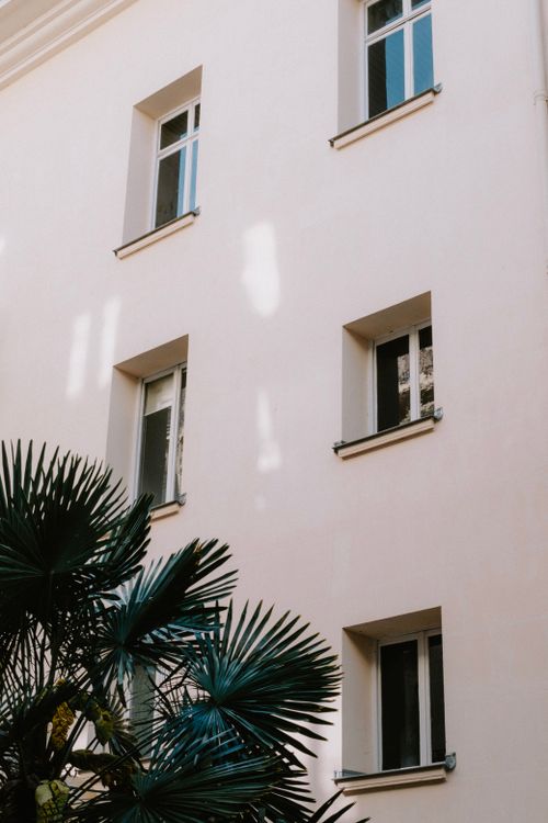 Free Elegant white building exterior with multiple windows, complemented by greenery, evoking a minimalist architectural aesthetic. Stock Photo