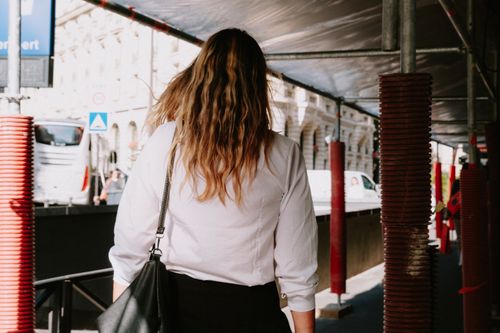 Free Rear view of woman in white shirt walking under scaffolding on a city street. Stock Photo
