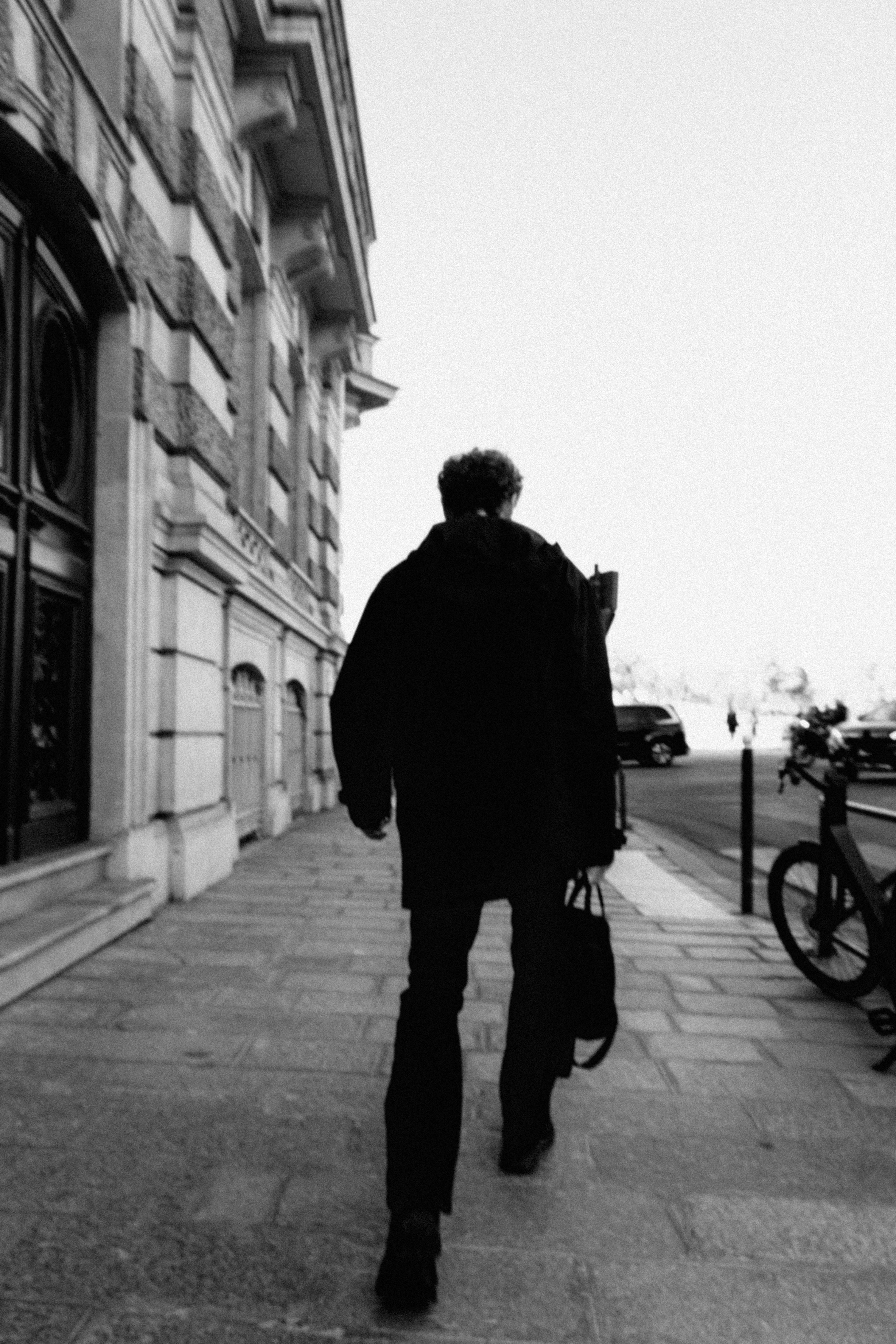 Free A solitary man walking on a city sidewalk, captured in black and white, creating a classic urban scene. Stock Photo