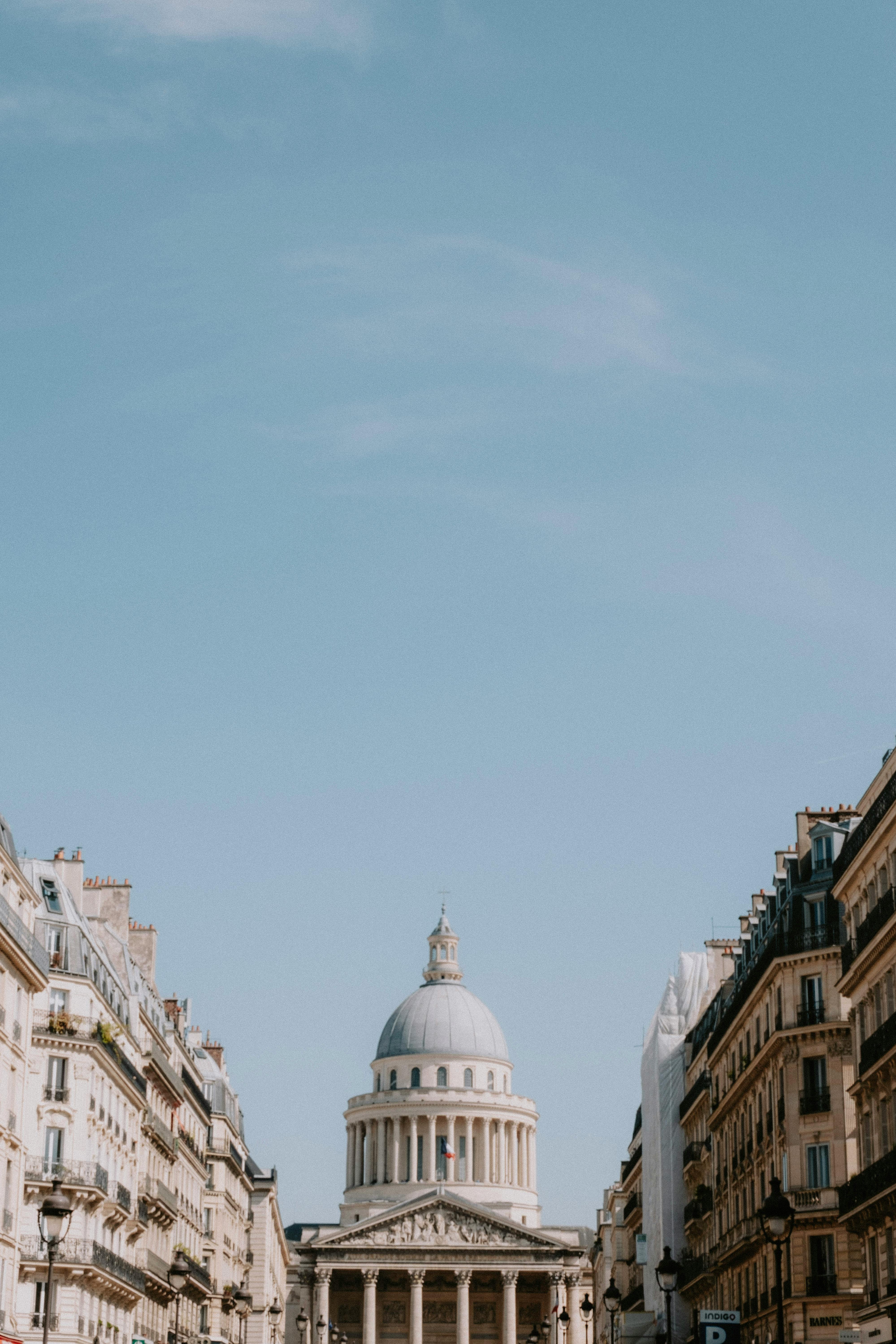 Capture of the Paris Pantheon framed by classic Parisian architecture under a clear sky.