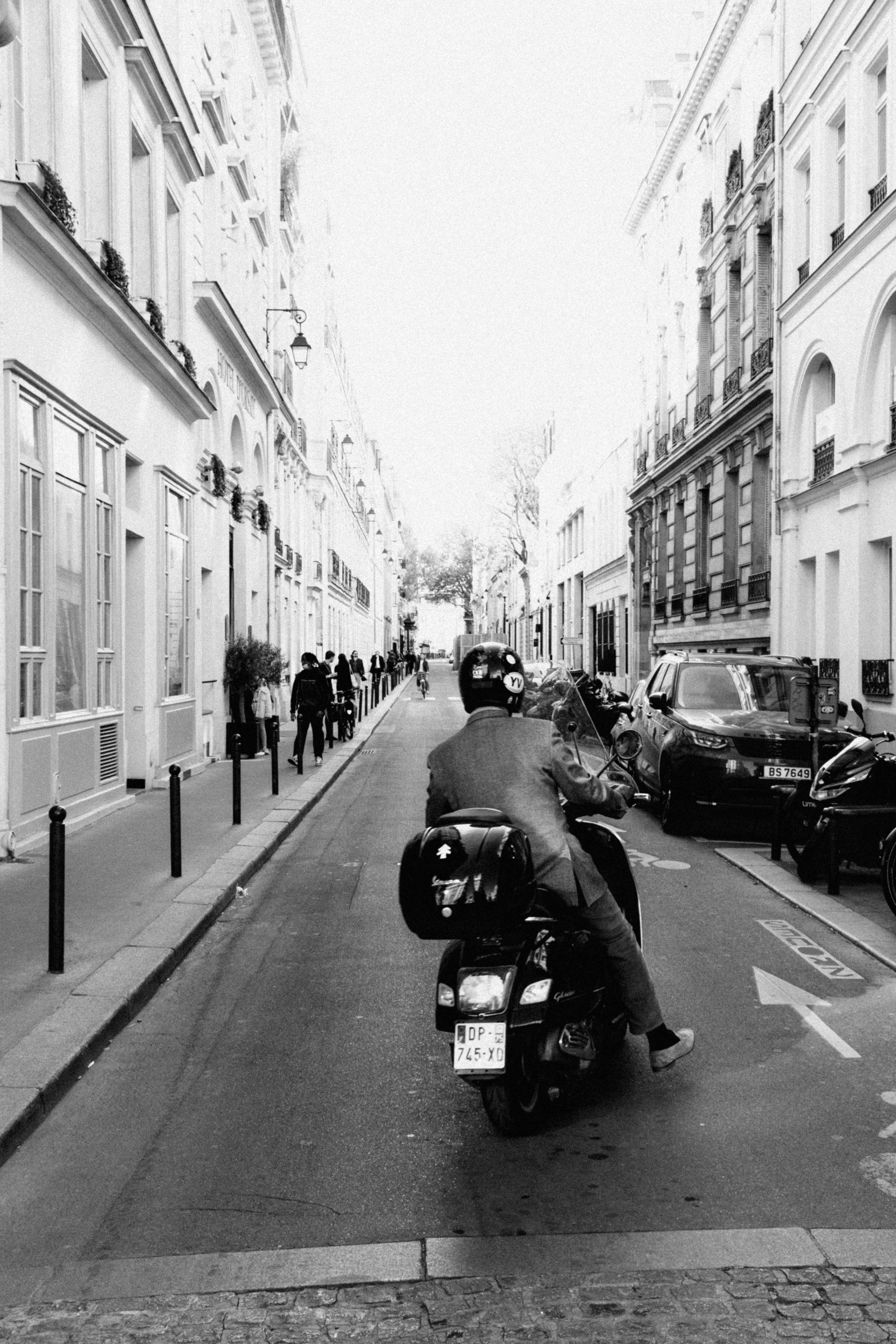 Motorcycle rider on a narrow urban street, black and white style.