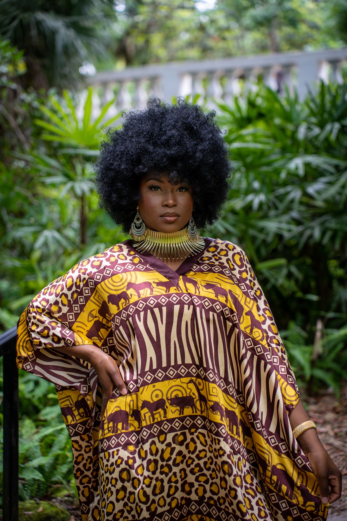 Woman with an afro in a patterned kaftan dress among tropical plants