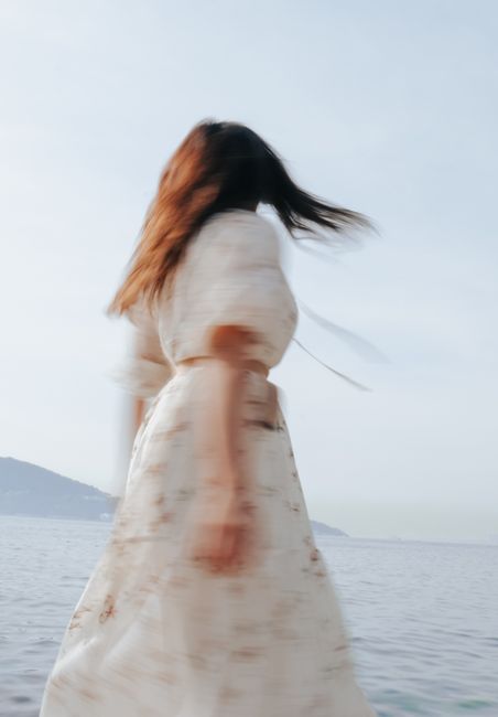 Blurred motion of a woman in white dress by the sea, capturing a dreamy, ethereal mood.