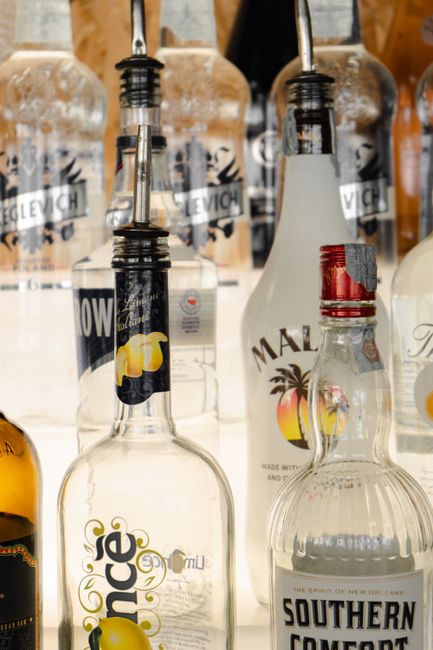 Photo by Natasha Filippovskaya Collection of glass liquor bottles with pour spouts on a shelf, showcasing various brands.