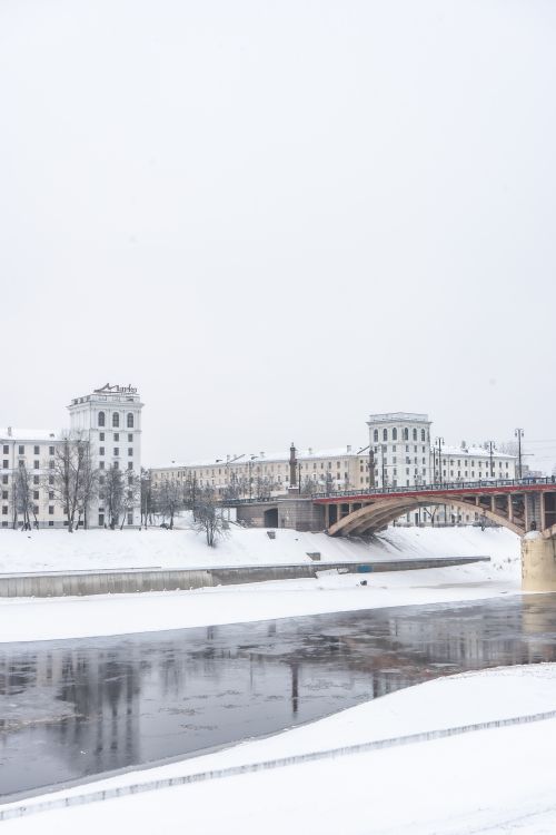 Free Scenic winter landscape of Vitebsk, Belarus featuring snow-covered buildings and a frozen river. Stock Photo