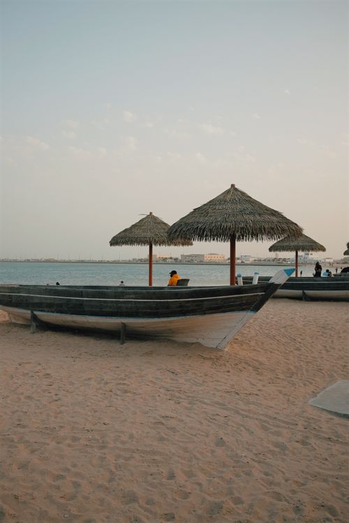 Free Serene sandy beach with wooden boats and thatched umbrellas by the calm sea. Stock Photo