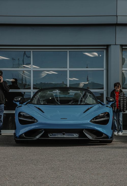 Free A sleek blue supercar parked in front of a glass garage with people around. Stock Photo