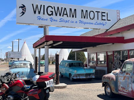 Vintage cars and Wigwam Motel sign in Holbrook, AZ, under a clear sky.
