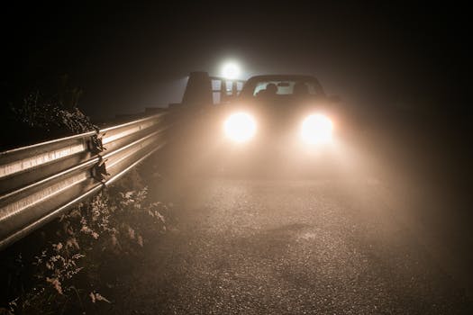 A mysterious car driving at night through foggy Coatepec, headlights illuminating the road.