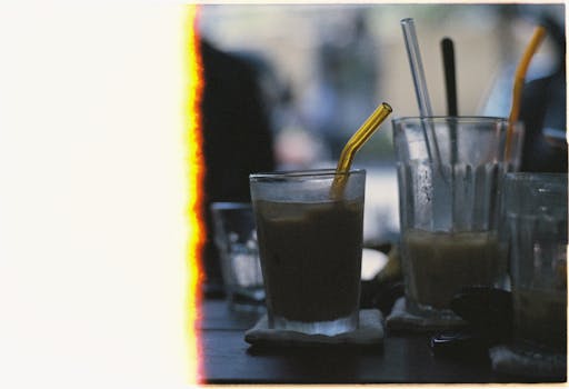 Retro film-like iced coffee scene with straws and dramatic light streaks.