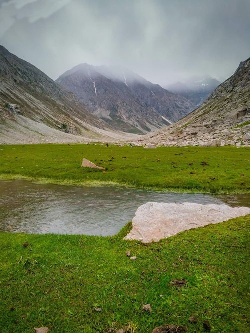 Free A peaceful mountain valley landscape in Pakistan featuring a tranquil lake and lush greenery under cloudy skies. Stock Photo