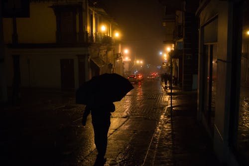 A Person Walking at Night Holding an Umbrella