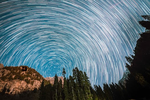 Long exposure capturing mesmerizing star trails above forested mountains at night.