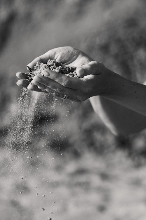 Grayscale Photo of a Person Holding Sand