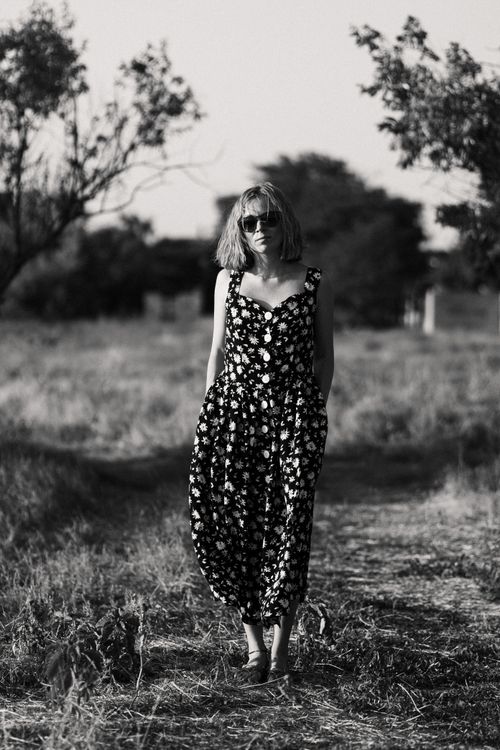 Free Black and white photo of a woman in a floral dress walking in a sunlit field. Stock Photo