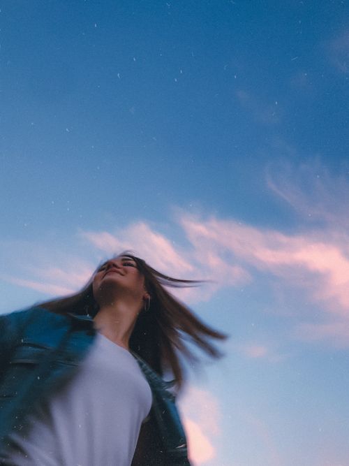 Free Blurred motion portrait of a woman in a blue jacket under a vibrant sky, conveying freedom. Stock Photo