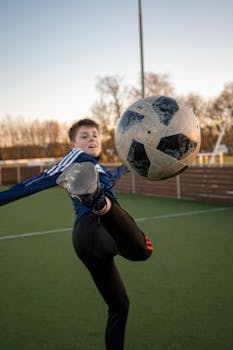 A teenager kicks a soccer ball on an outdoor field in Støvring, Denmark during sunset.