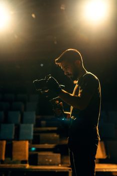 A filmmaker adjusts his camera under bright stage spotlights, creating a dramatic scene.