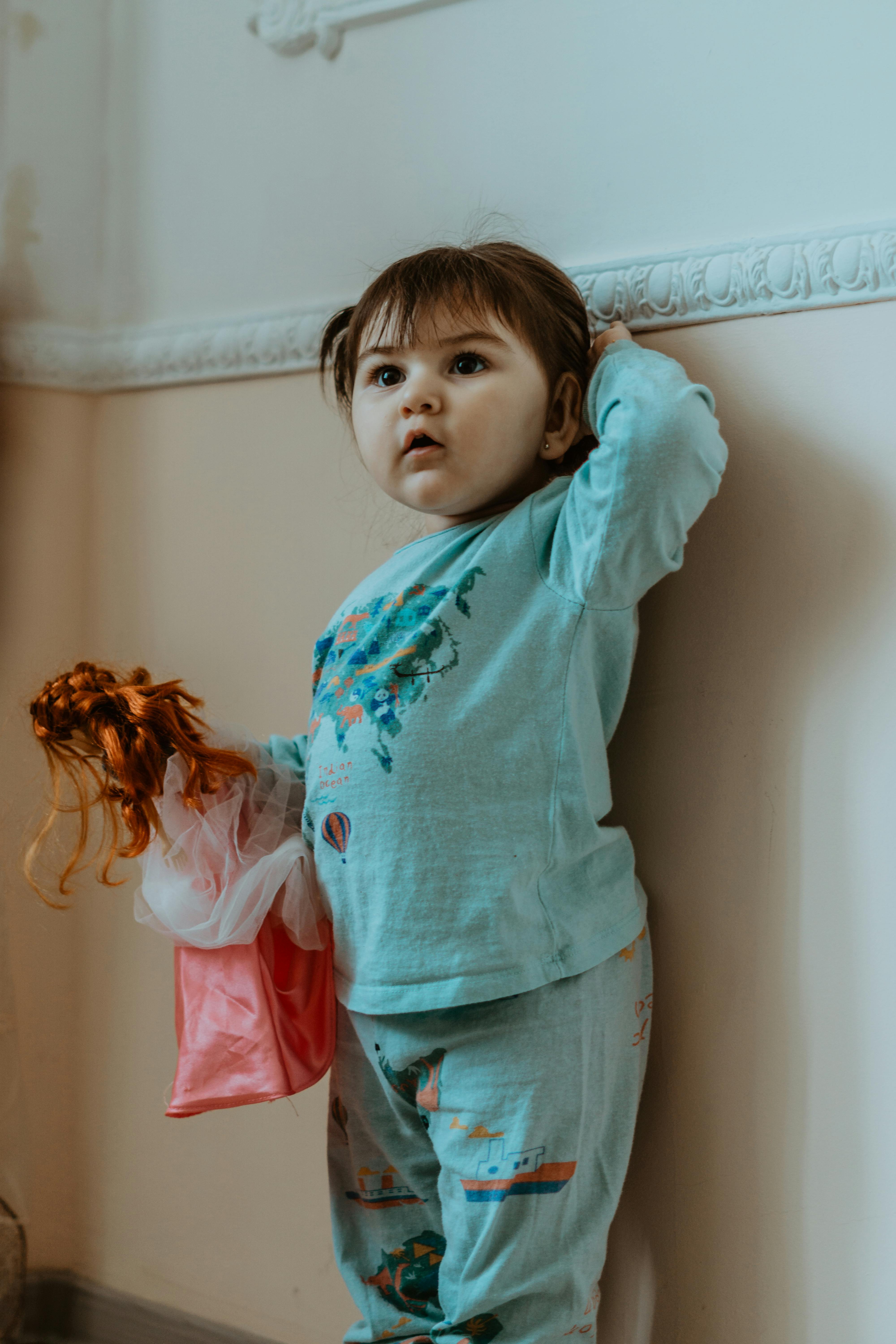 a girl standing against a wall holding a doll