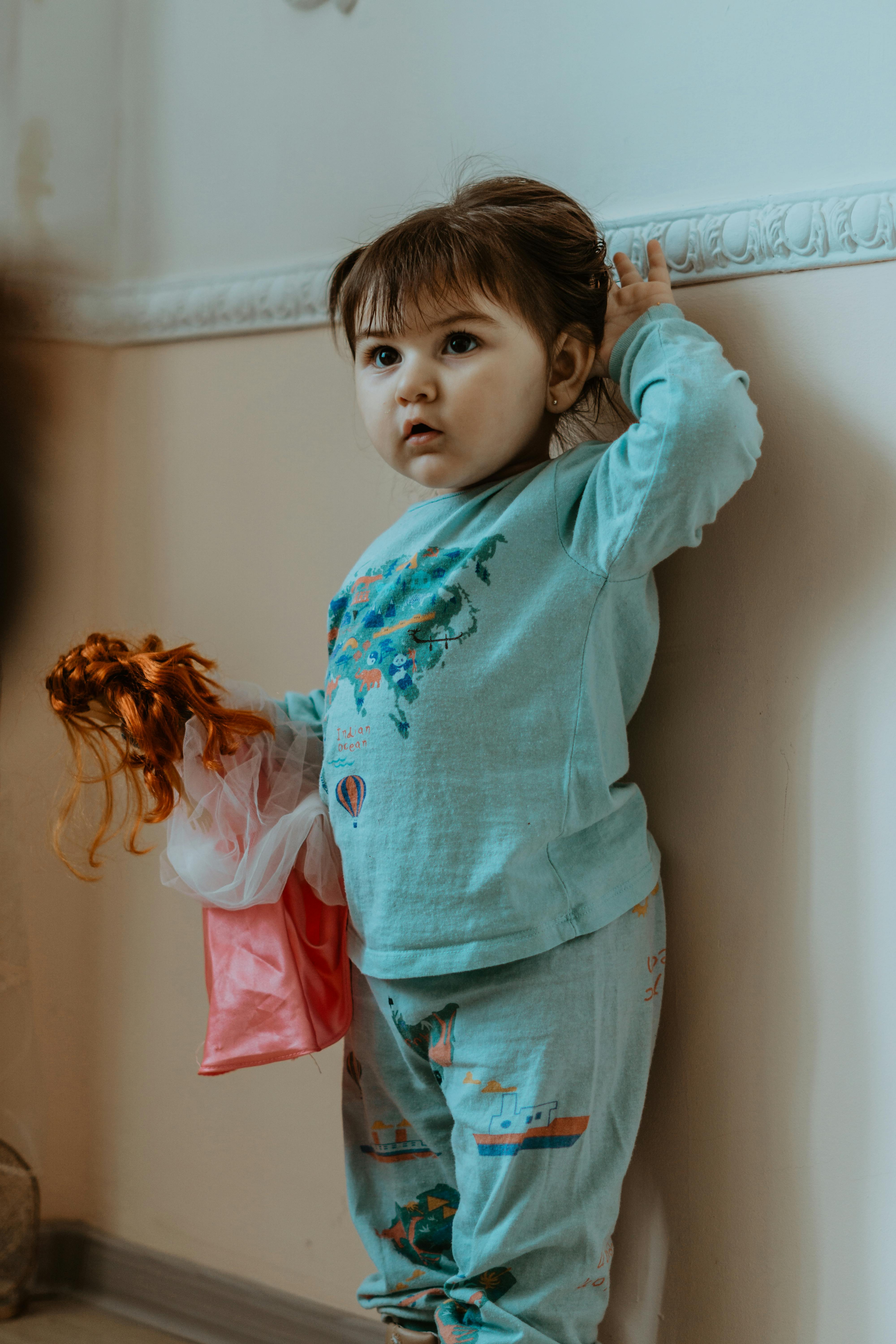 a girl holding a doll while leaning on the wall