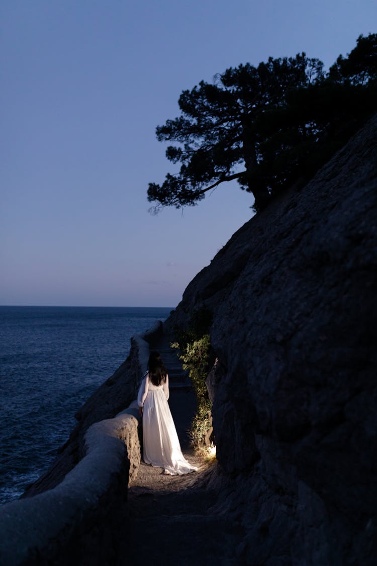 Woman In A Long White Dress Looking At Sea From A Cliff