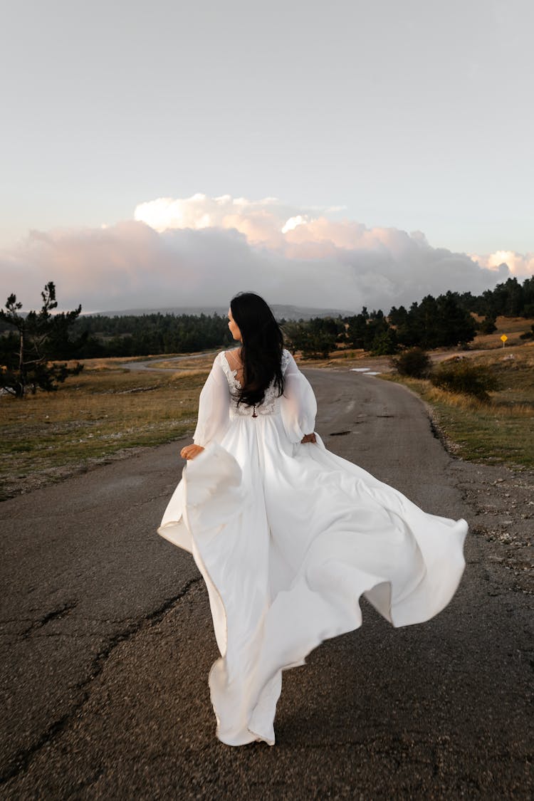 Back Of A Woman Walking Down The Road In A Gown