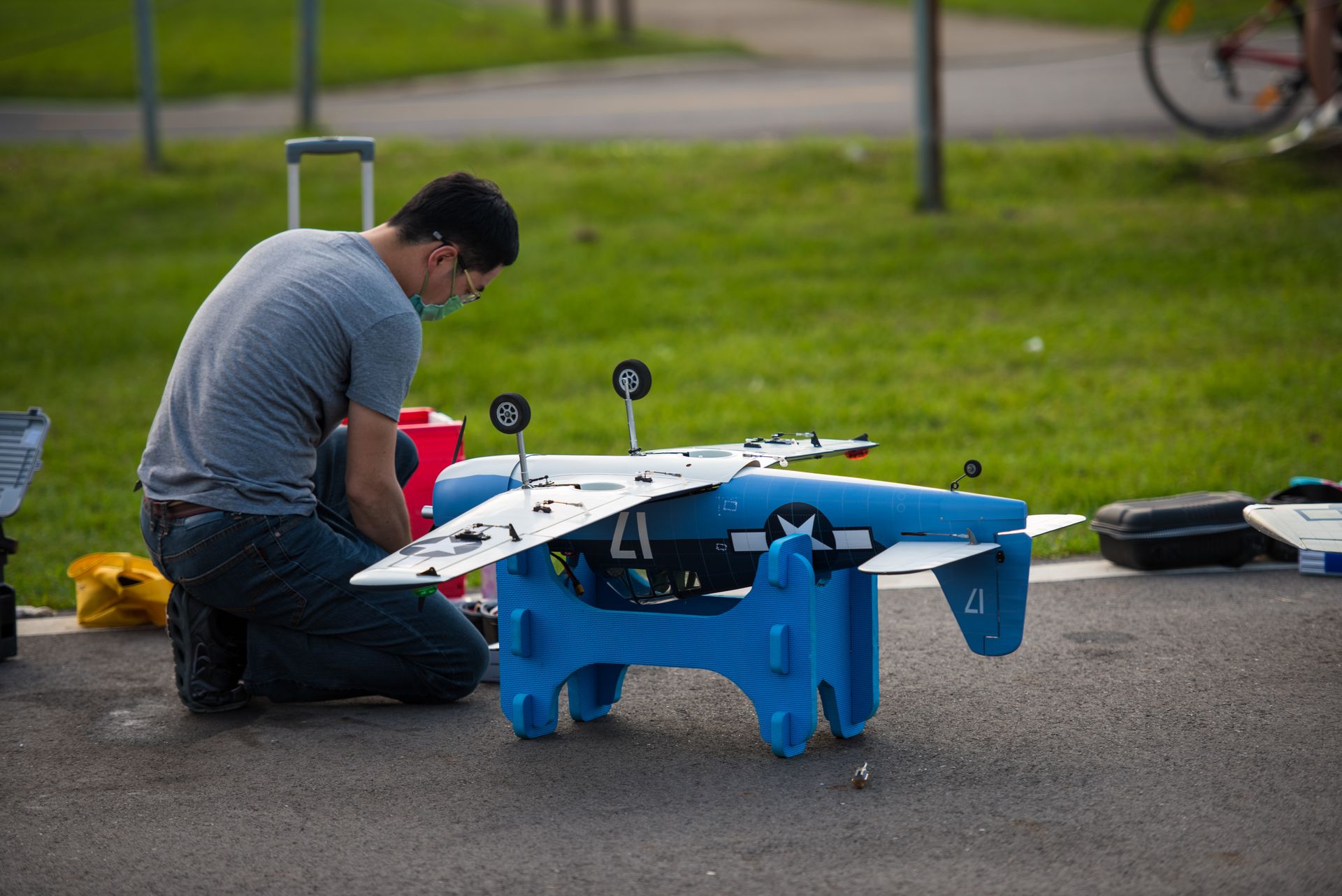 Man repairing a remote controlled model aircraft outdoors on a sunny day.