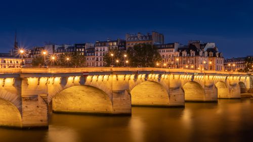 Free Illuminated Pont Neuf bridge reflecting on the Seine River at night in Paris, creating a serene cityscape. Stock Photo