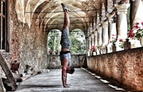 一名男子在一条有砖墙和鲜花的乡村拱廊里倒立