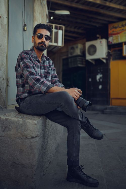 Free Casual photographer with glasses sitting outdoors in Iran, holding a camera. Stock Photo