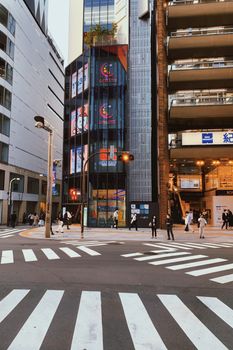 A bustling street scene at a busy Japanese intersection with modern buildings and zebra crossing.