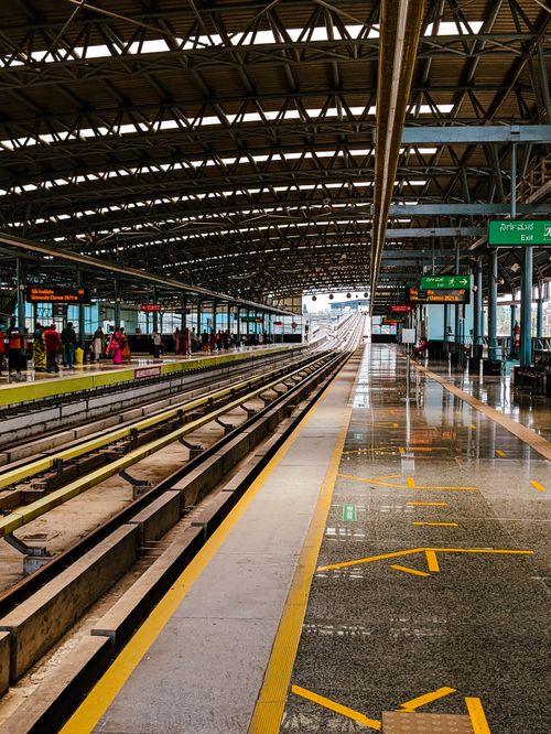 Free Bright view of a train station in Bengaluru, featuring empty tracks and a few people on the platform. Stock Photo