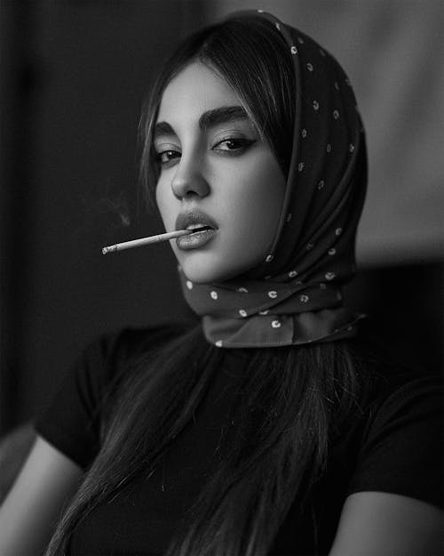 A Grayscale Photo of a Woman in Black Shirt Smoking Cigarette
