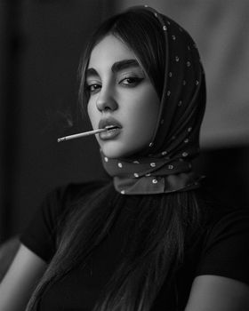 Artistic monochrome portrait of a woman in a headscarf with cigarette.