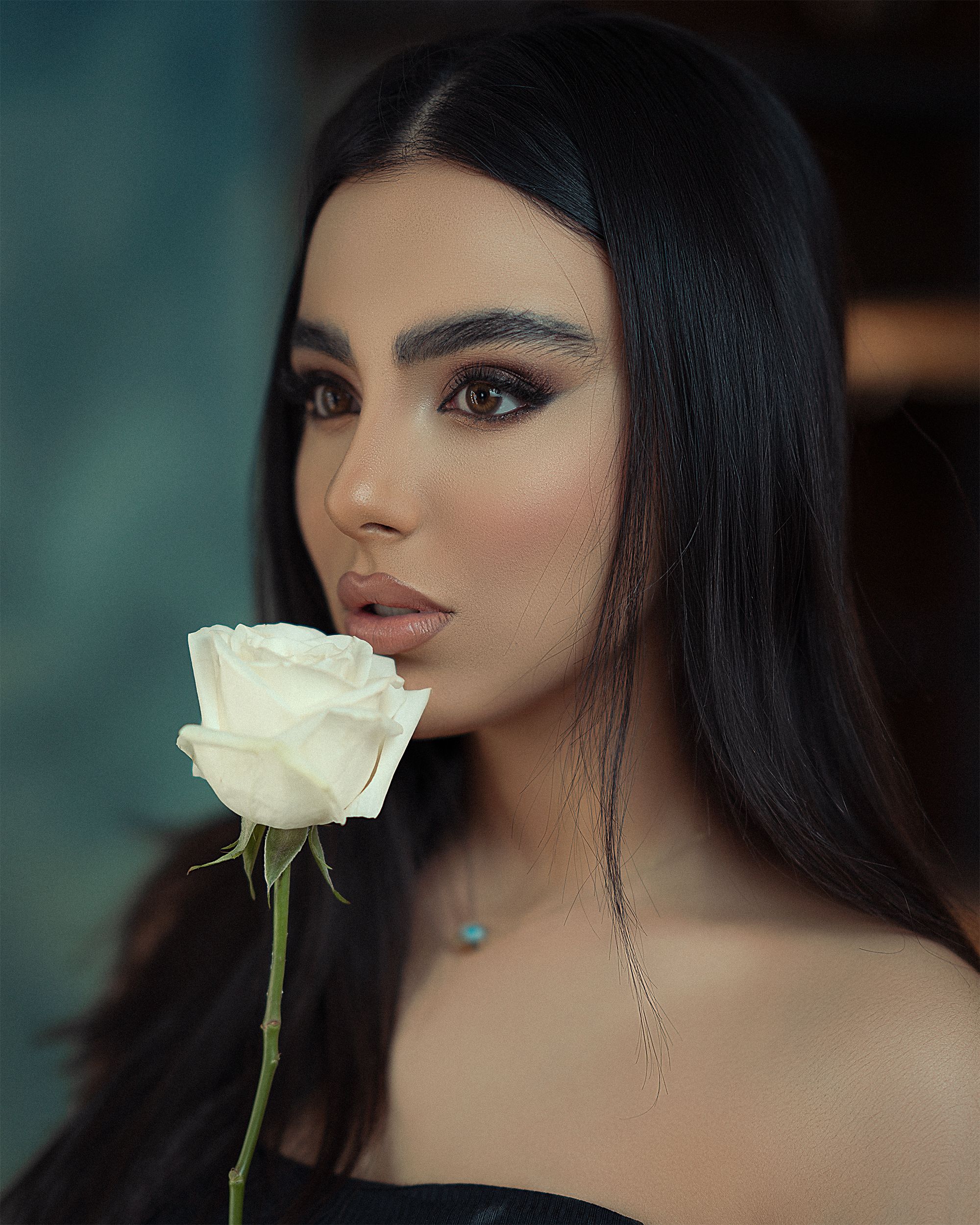 Close-up portrait of a brunette woman holding a white rose with a glamorous expression.