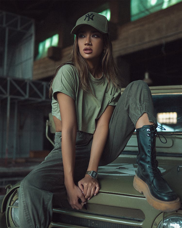 Woman In Green Crop Top Wearing Black Boots Sitting On The Hood Of A Car While Looking Afar