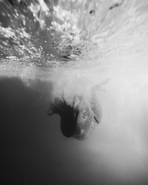 Artistic black and white underwater photo of a woman diving with flowing hair.
