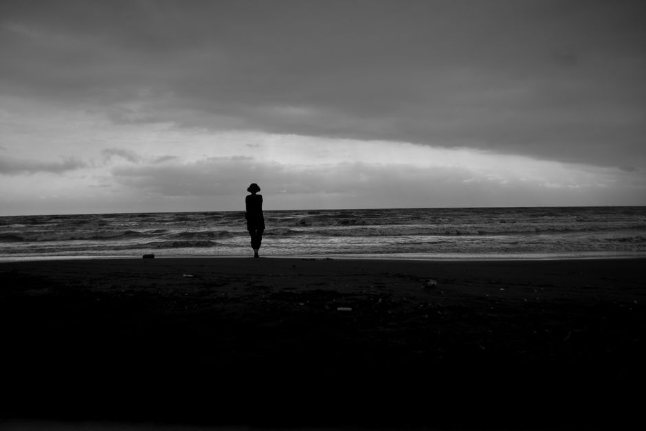 A serene black and white image of a silhouette person on a beach with a cloudy sky.