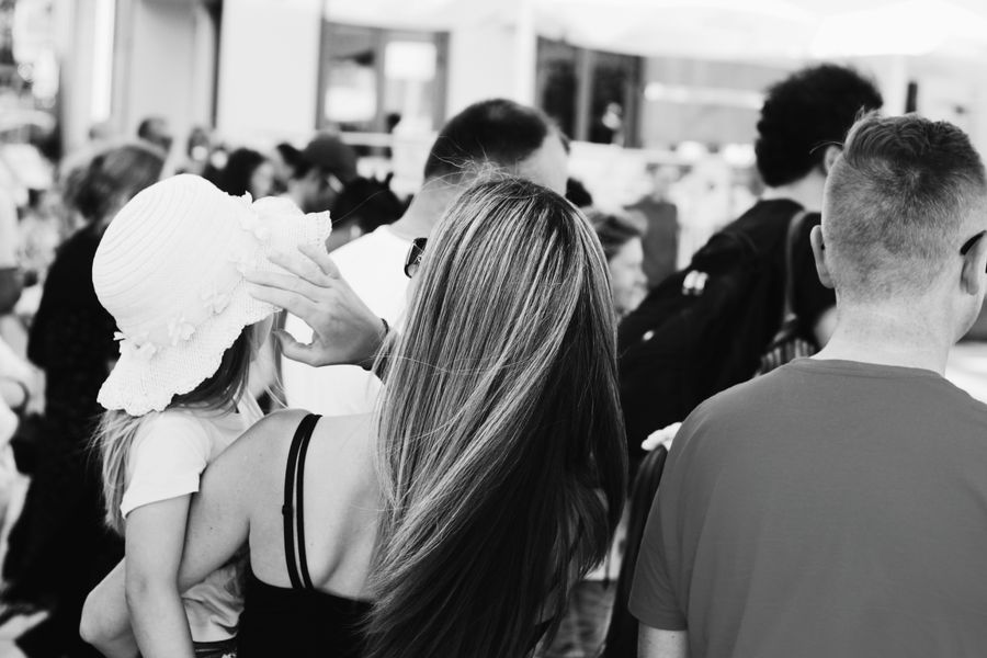 Monochrome photo showing mother holding child in a crowded place, facing away.