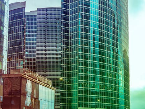 明亮的天空下，现代摩天大楼的反光玻璃外墙映衬出动态的城市景观