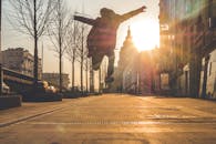 日落时分，一名男子的剪影在城市街道上迎着明媚的阳光精力充沛地跳跃