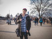 白天，一个穿着格子衬衫、戴着帽子的年轻人在繁华的城市公园里悠闲地散步