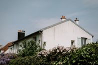 Rustic cottage with a pitched roof and blooming flowers against a clear sky.