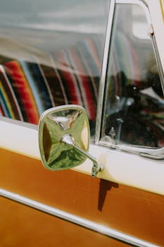Close-up of a vintage car's side mirror with colorful interior reflection, captured outdoors.