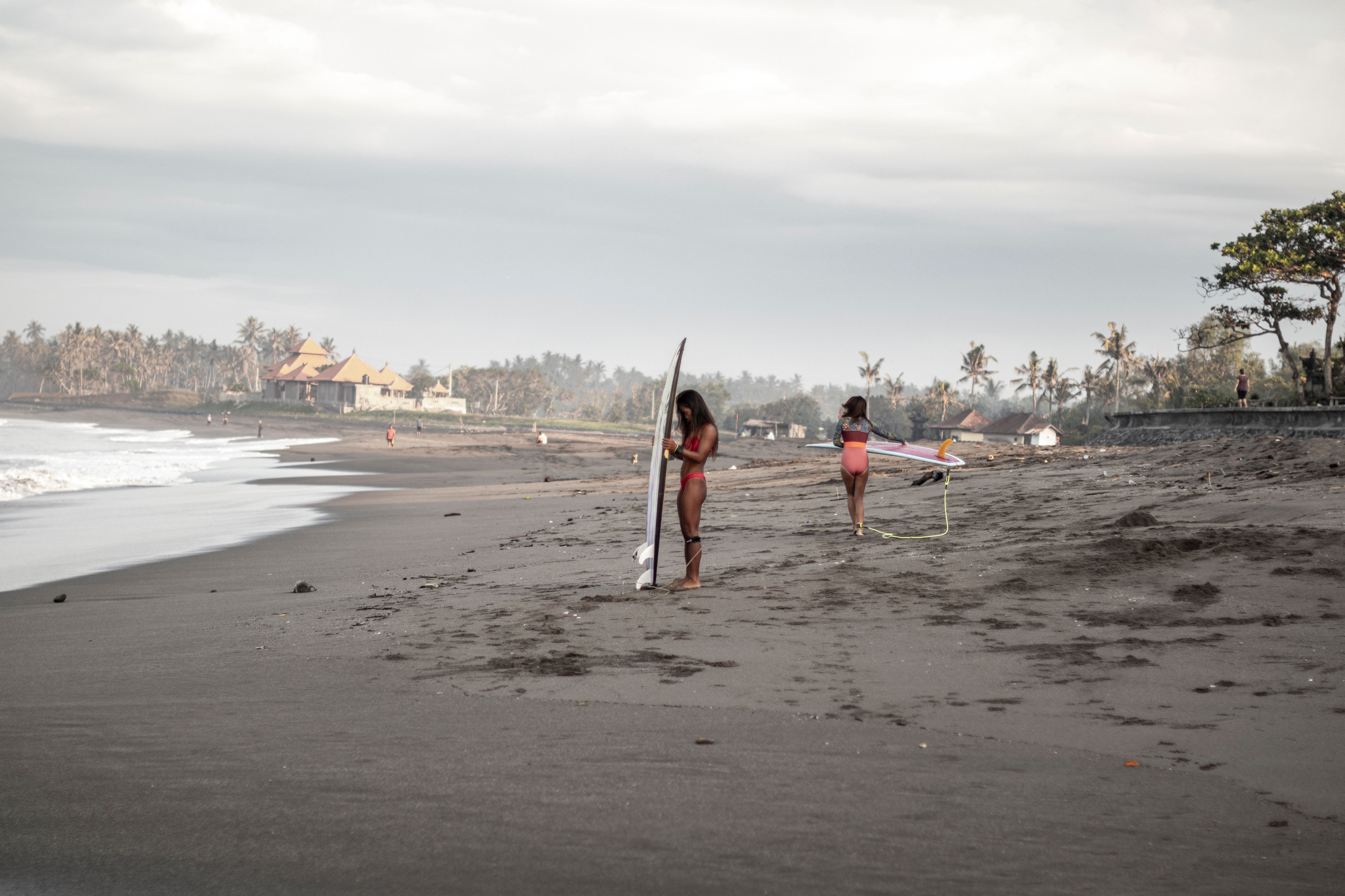 Two women with surfboards on a tropical beach at sunrise, preparing for surfing adventure.