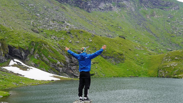 A Person Wearing A Blue Jacket Standing On The Edge Of A Cliff With Arms Outstretched