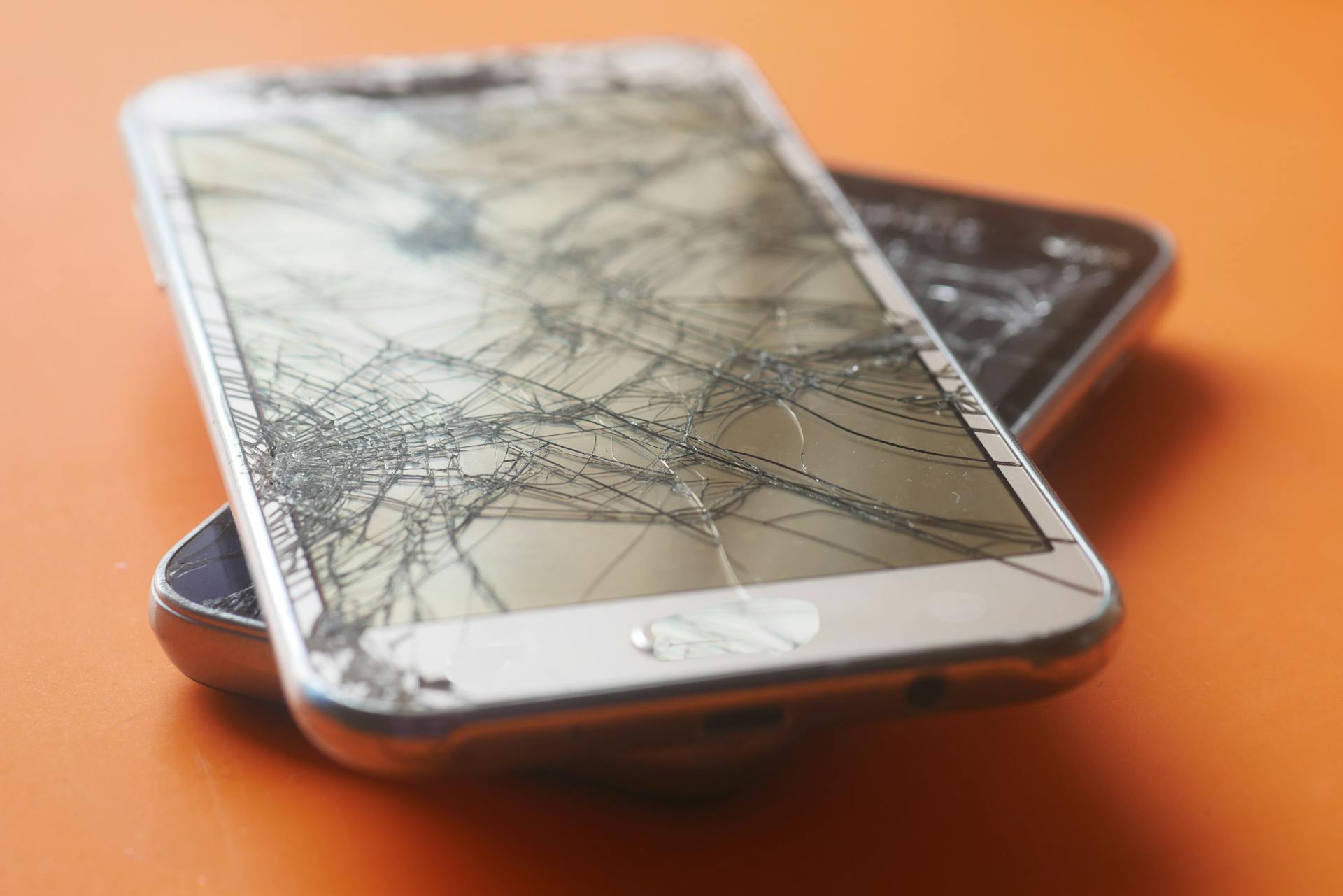 Two broken smartphone screens on an orange background, illustrating device fragility.