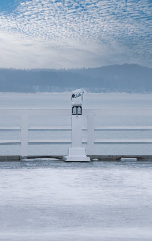 A Telescope on a Pier with View of a Body of Water and Hills